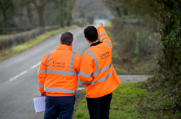 county broadband engineers wearing orange jackets point at a road