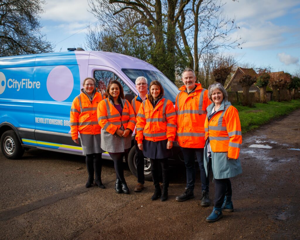 Lucy Frazer MP with CityFibre staff, standing in front of a CityFibre-branded van. They are all wearing hi-vis jackets and smiling.