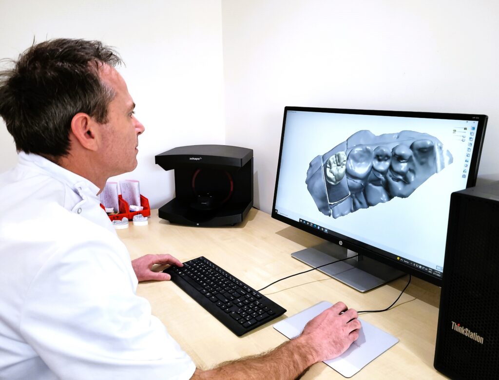 Stefan the dental technician is sitting at a computer looking at an impression of teeth on the screen.