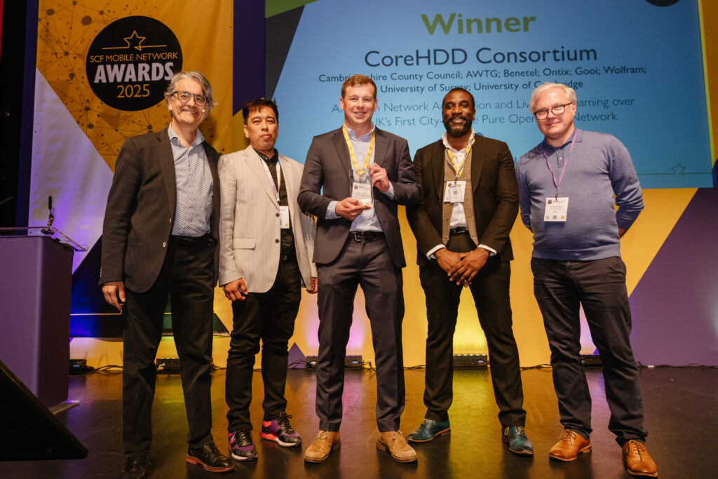 Photo shows MIchael Stevens of Connecting Cambridgeshire on stage collecting the Small Cell Forum award with Ian Vernon (AWTG Ltd), David Mintah (AWTG Ltd) and Andrew Thomas (Benetel).