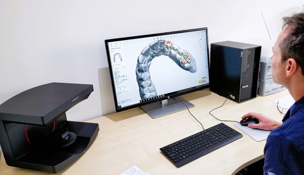 Stefan the dental technician is sitting at a computer with the digital scanner next to him.